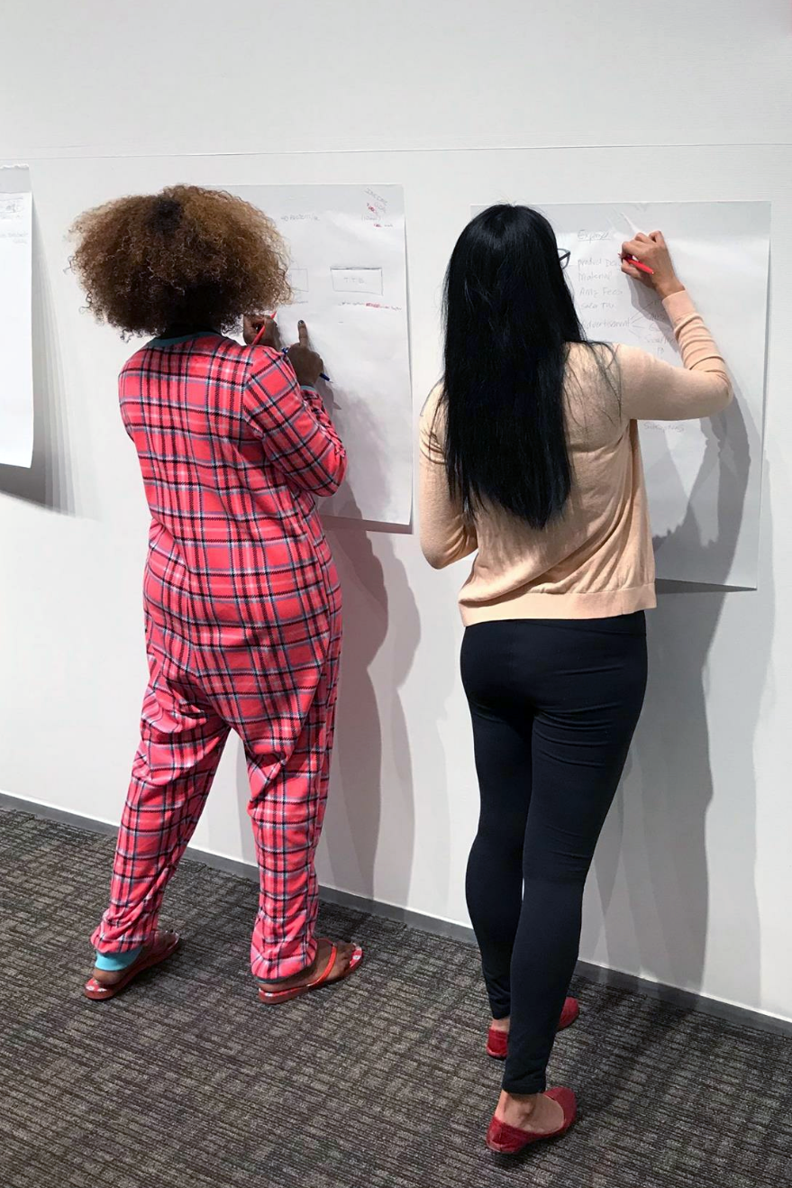 Paula Kinney, who owns an interior design business and is the emcee for BizChix Live 2018, dressed in a pink onesie and writing on white paper on the wall. 